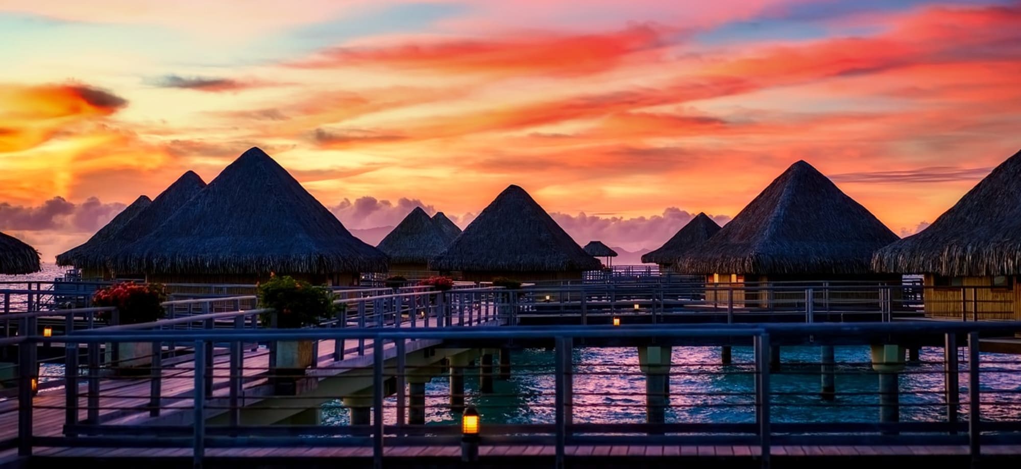 The sun has set, cascading orange and yellow hues across the sky and the overwater villas are purple. 
